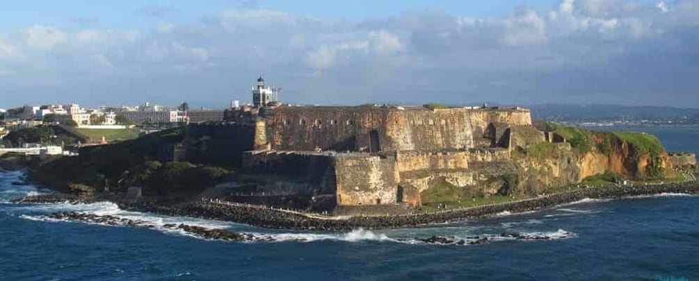 A coastal fortification with a lighthouse, surrounded by water and a distant cityscape. 1