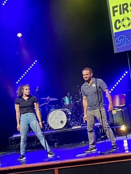 Two people on a stage with musical instruments, under blue stage lighting. 3