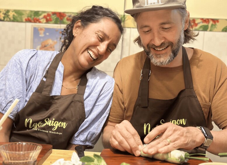 Two people wearing aprons with 'Ng Saigon' text, working with vegetables on a wooden table. 1