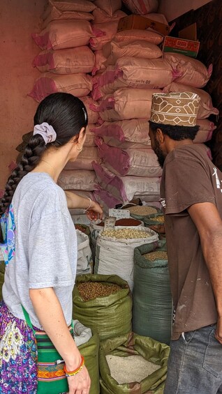 Two people at a market stall with sacks of grains and a price sign. 2