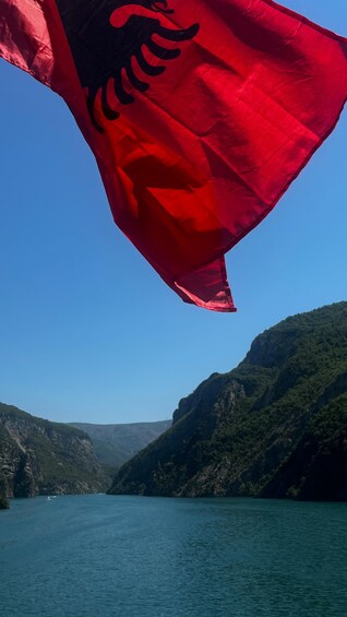 A red flag with a black design, a clear blue sky, and a mountainous landscape with a body of water. 4