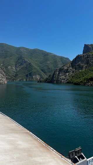 A calm lake surrounded by green hills and a rocky cliff. 3