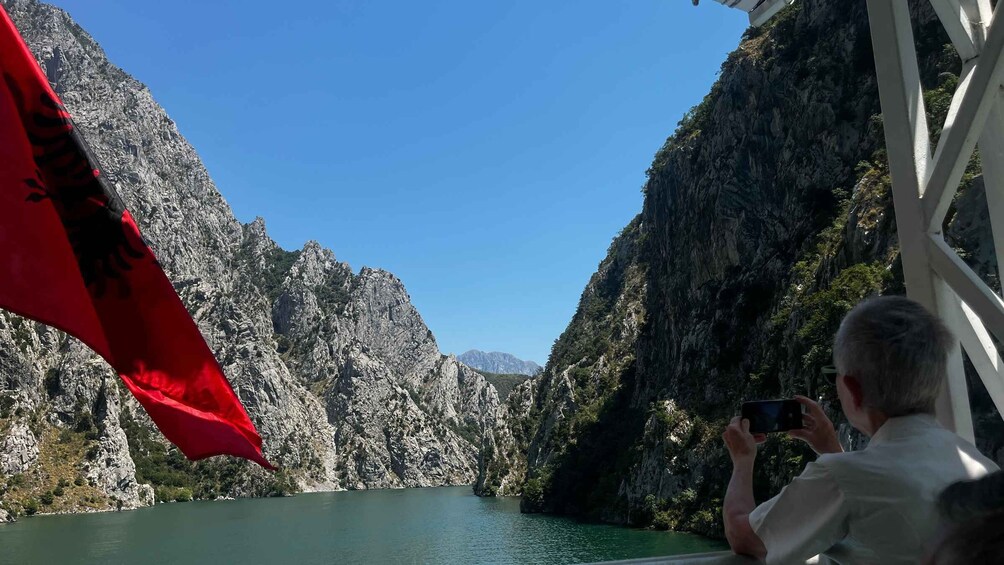 A person taking a photo of a mountainous landscape with a body of water. 1