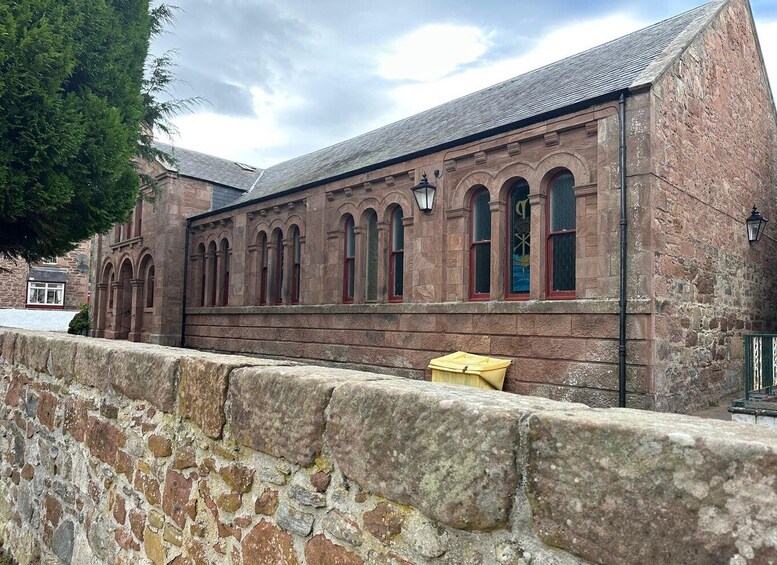 A historic stone building with arched windows and a stone wall in the foreground. 5