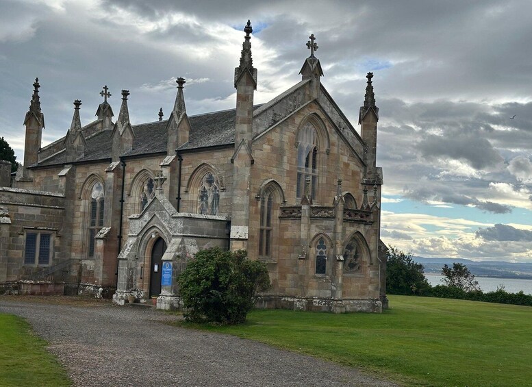 A historic church with Gothic architecture, a gravel driveway, and a body of water in the background. 5