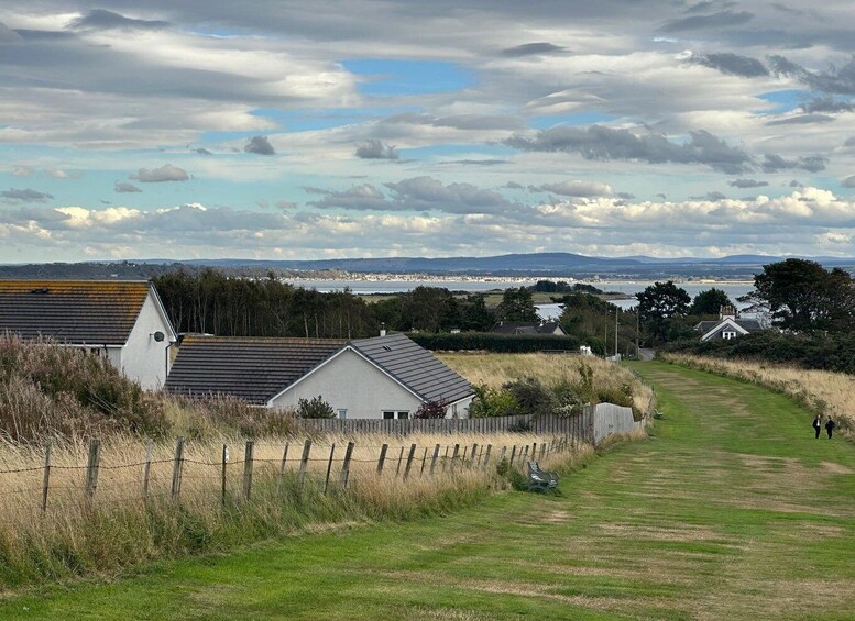 A rural landscape with houses, a grassy path, and a distant view of a town and hills. 3