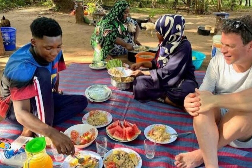 People sitting on a blanket outdoors, eating various dishes. 1
