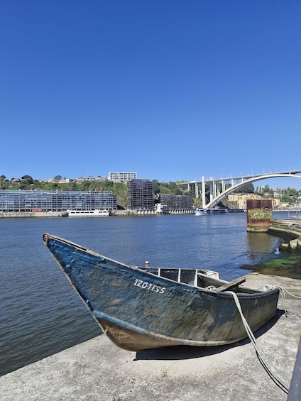 A blue boat with '1201ES5' on its side docked at a pier, a bridge in the background, and buildings along the riverbank. 1