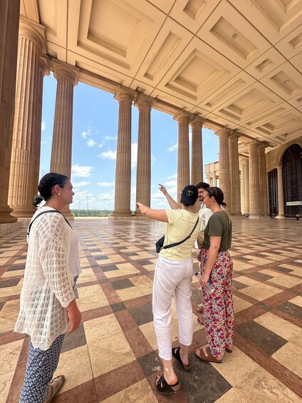 A group of people standing in a large, open hall with high ceilings and large columns. 2