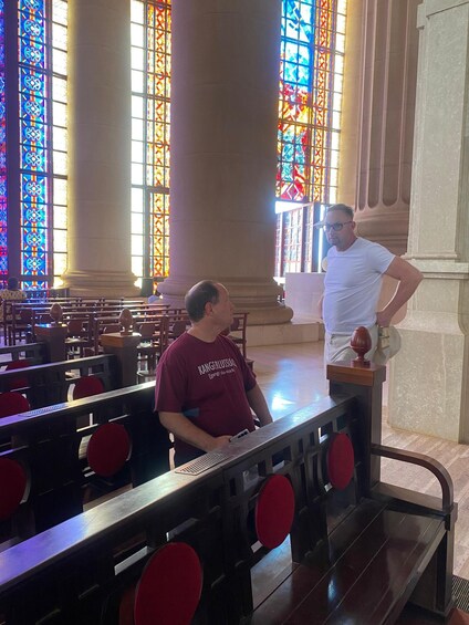A church interior with stained glass windows, wooden pews, and a man standing by a lectern. 5