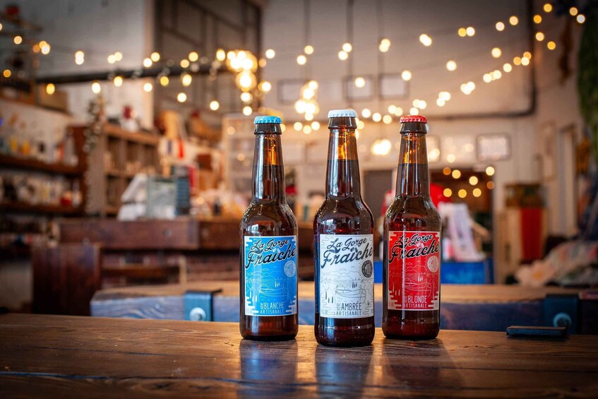 Three bottles of La Grosse Fraiche beer on a wooden table with a blurred background of a bar or restaurant. 1