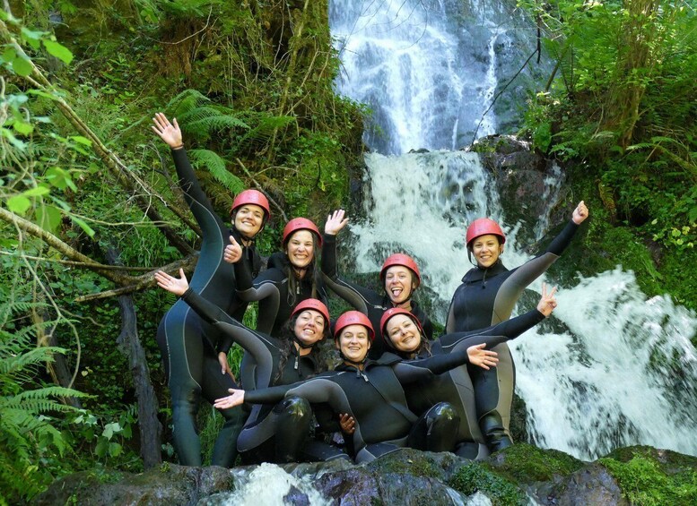 A group of people in wetsuits and helmets posing in front of a waterfall. 1