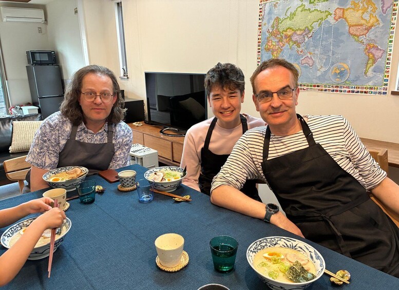 Four people sitting at a table with bowls of food, a map on the wall, and a television in the background. 2