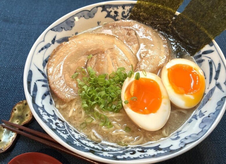 A bowl of ramen with sliced pork, two halves of a boiled egg, and chopped green onions. 1