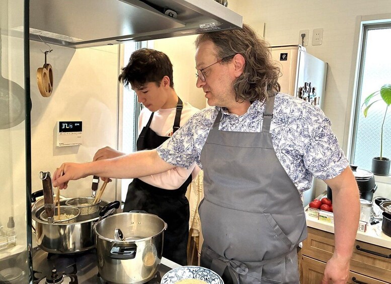 Two individuals cooking in a kitchen with stainless steel pots and a wooden spoon. 4