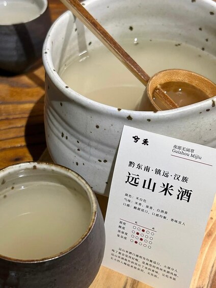 Two ceramic pots with a wooden spoon, one filled with a clear liquid, and a menu with Chinese characters. 3