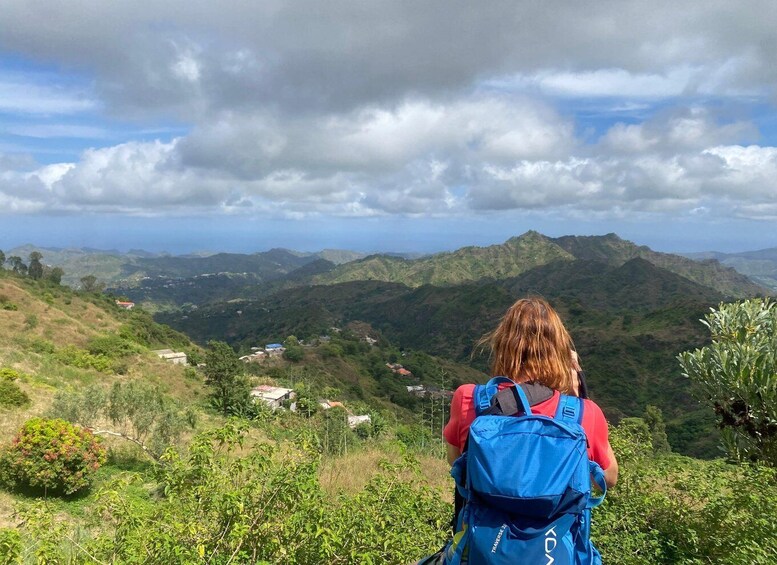 A person with a blue backpack overlooking a mountainous landscape with scattered houses. 5