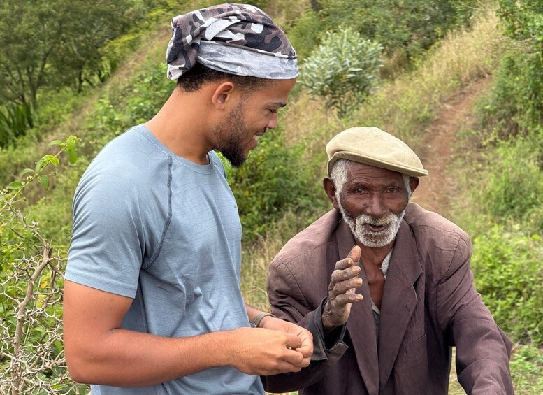 Two men in a natural setting with greenery and a dirt path. 1