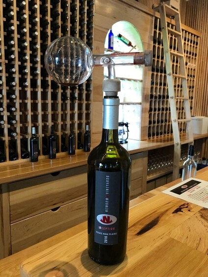 A bottle of wine with a label indicating 'Inception Texas High Plains 2016' on a wooden counter in a wine cellar. 5