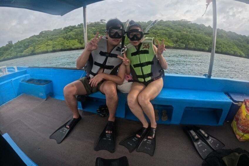 Two people on a boat wearing life jackets and flippers, with a body of water and greenery in the background. 4