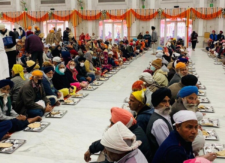 A large group of people seated in rows, some wearing turbans, in a hall with orange drapes. 4
