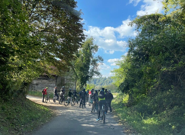 A group of cyclists on a paved path surrounded by trees and a stone building. 3