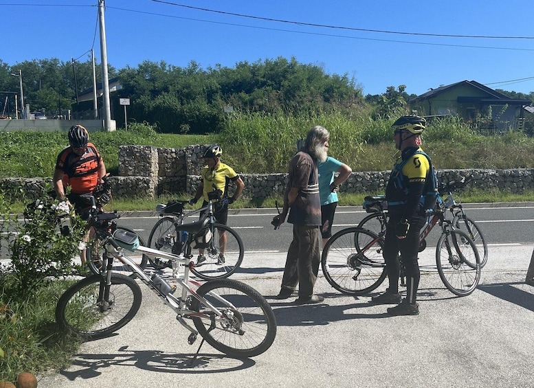 A group of cyclists on a paved road with a stone wall and greenery in the background. 1