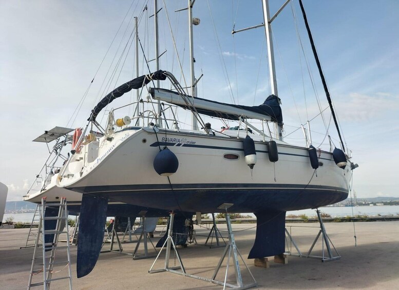 A sailboat named 'BAVARIA 46 cruiser' on a dry dock with its hull elevated and supported by metal stands. 5