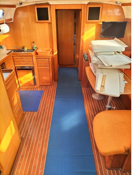 A narrow corridor with wooden walls, a blue mat, a bench, and a small kitchenette. 2