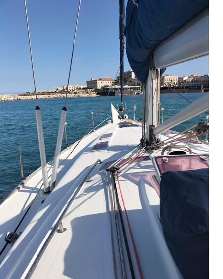 A sailboat's deck with masts, ropes, and a view of the coastline. 1