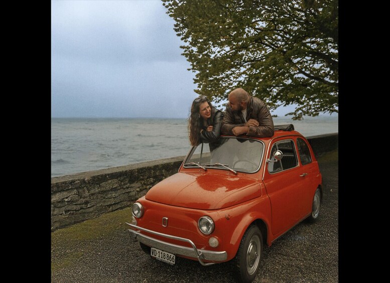 A red vintage car parked by the seaside with a rocky wall and a tree in the background. 3