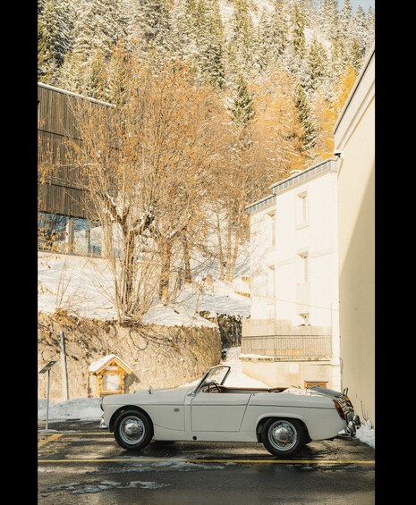 A white convertible parked on a snow-covered street, with a building and trees in the background. 5
