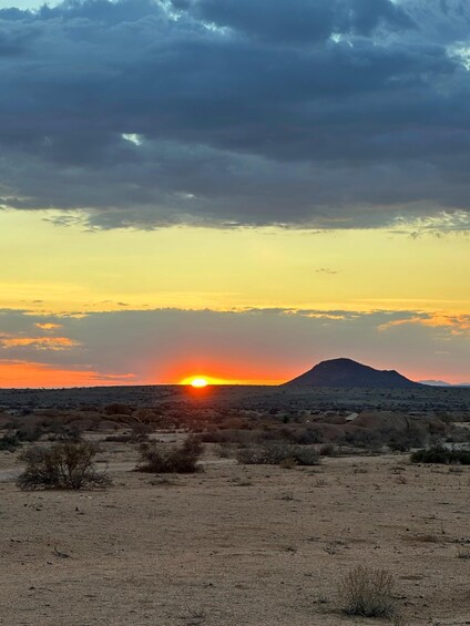 A desert landscape at sunset with a mountain in the distance. 1