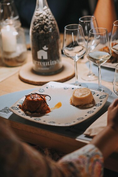 A dessert plate with a caramel flan and a chocolate sauce garnish, accompanied by wine glasses on a wooden table. 5