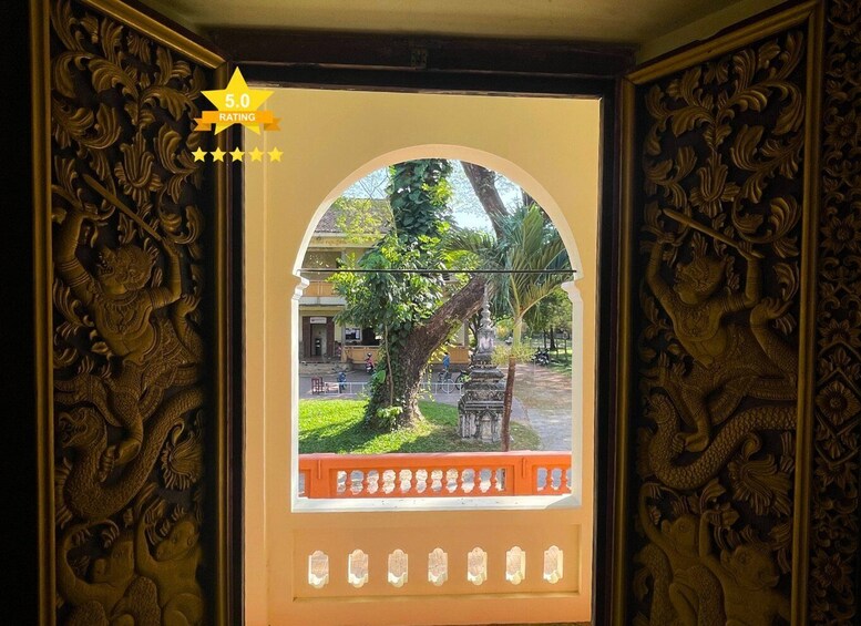 A framed view of a street scene with ornate carvings on the frame, a tree, and a building in the background. 2