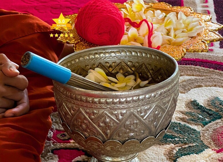 A hand holding a blue-handled whisk, a red ball of yarn, and a bowl with white flowers and a golden ornament. 3