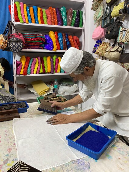 A person working with colorful fabric rolls and a blue container on a table. 5