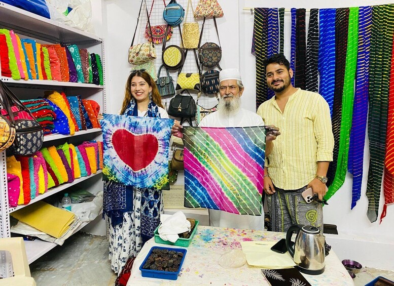 A craft workshop with colorful fabrics, a heart-shaped artwork, and a man holding a phone. 1