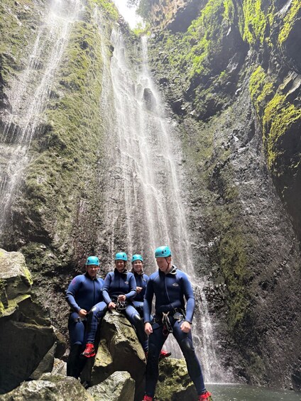 A group of people in blue wetsuits and helmets sitting on rocks by a waterfall. 5