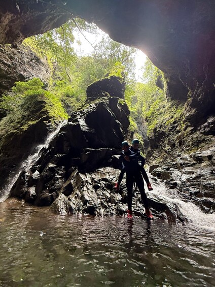 Two people standing on rocks by a waterfall in a forested gorge. 5