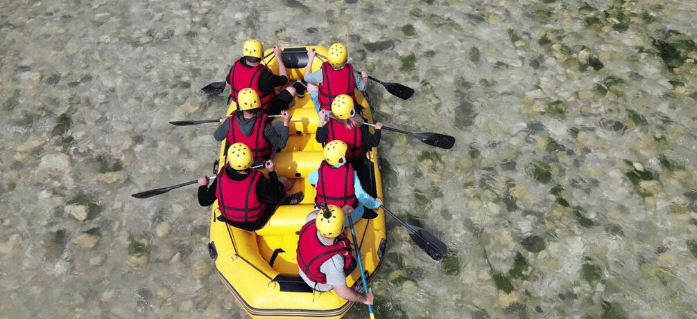 A group of people in a yellow raft with helmets, paddles, and life jackets. 3