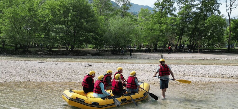 A group of people in a yellow inflatable raft on a river, wearing life jackets and helmets. 4