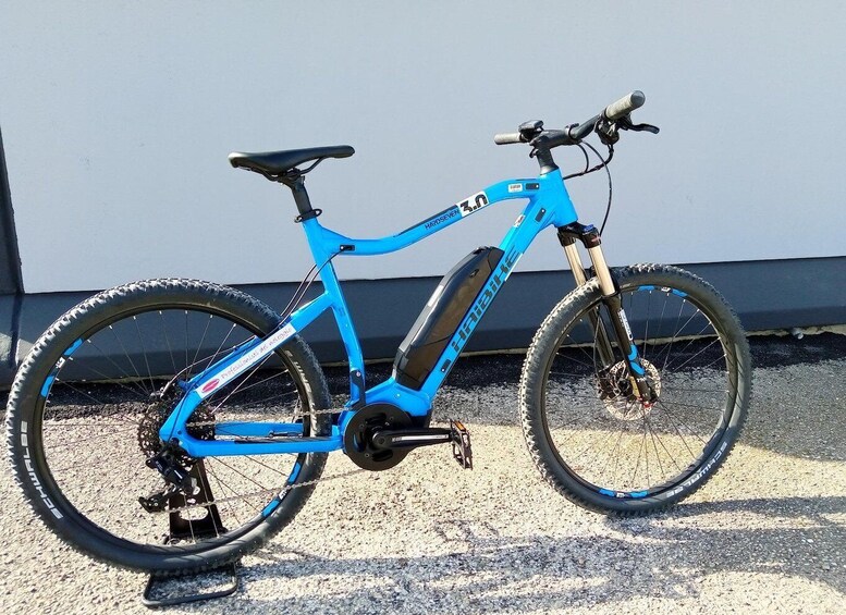 A blue electric bicycle with a black seat and front suspension fork, parked on gravel. 1