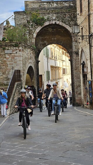 A group of cyclists riding through an ancient stone archway in a historic town. 3