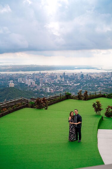 A couple standing on a green lawn with a cityscape in the background. 3