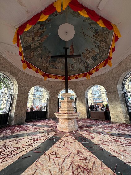 An ornate church interior with a central cross, stained glass windows, and a patterned floor. 4
