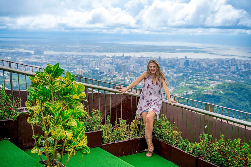 A person on a balcony with a cityscape in the background. 1