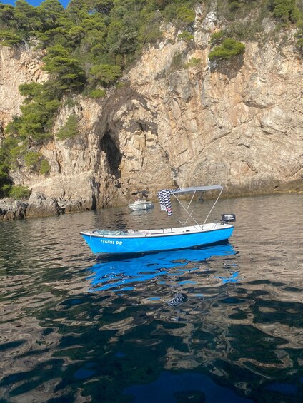 A blue boat with registration number 476581 DB anchored near a rocky cliff with sparse vegetation. 4