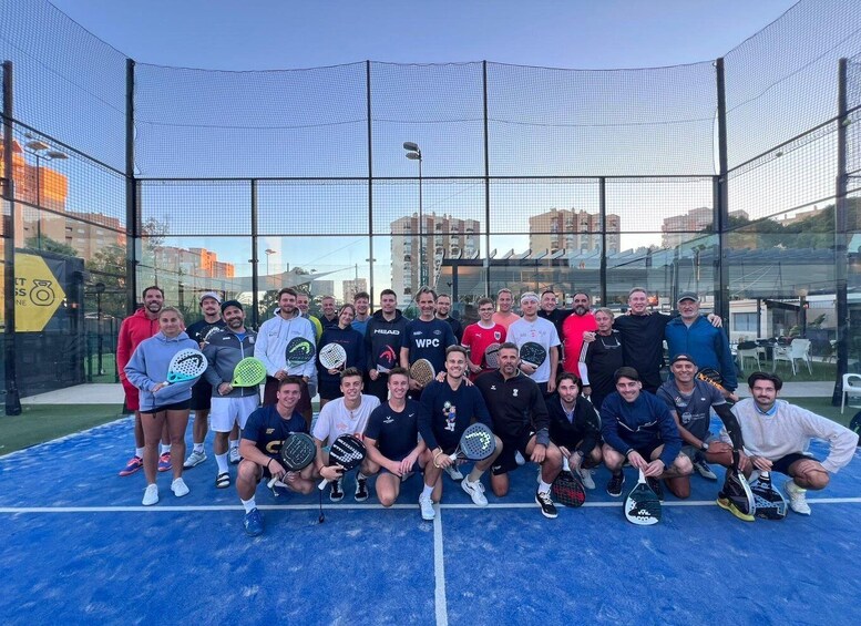 A group of people on a tennis court with a net and a glass wall in the background. 2