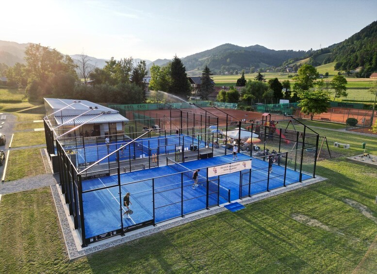 A tennis court surrounded by a fence, with a building and trees in the background. 1